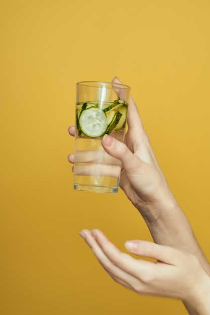 Girl with a glass of water with a cucumber on a yellow background studio