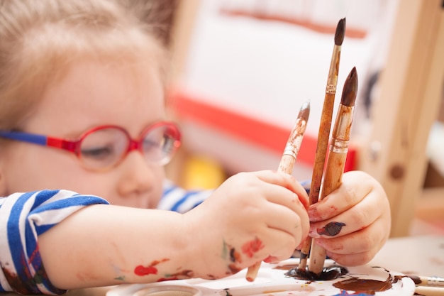 Girl with glasses is considering a brush and paint