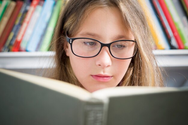 A girl with glasses is reading a book. 