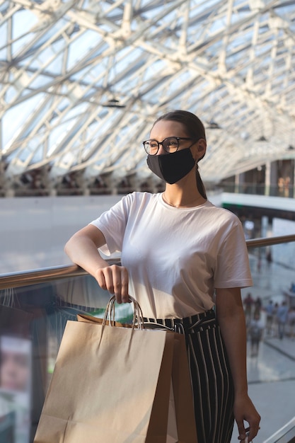 Girl with glasses and a protective mask in a mall with purchases