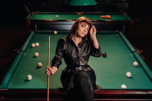 A girl with glasses sits on a pool table in a club