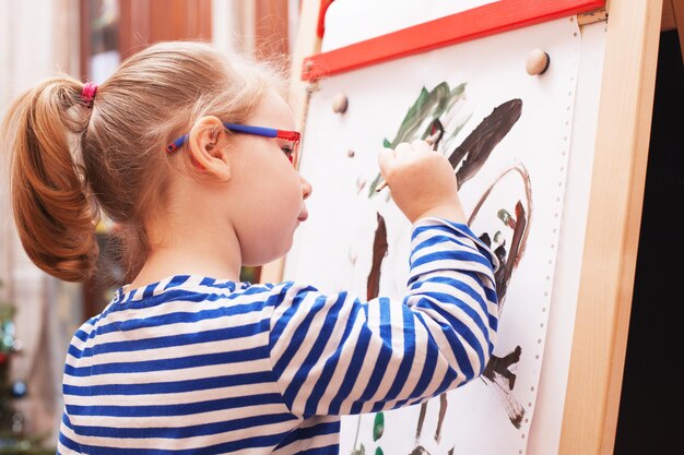 Photo girl with glasses and a striped t-shirt paints draws paints on white  canvas