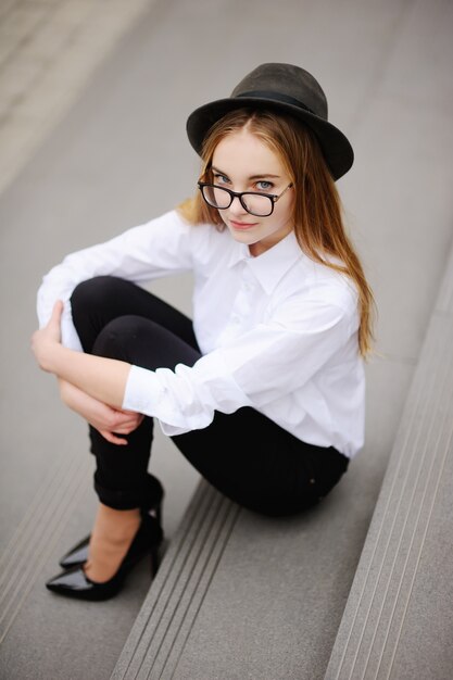 Ragazza con gli occhiali e cappello vintage seduto sui gradini