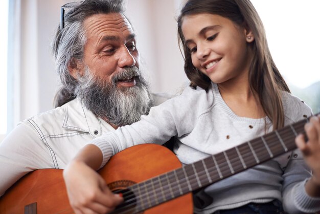 Girl with grandfather happy with guitar and learning to play music education and creative development Musician art and old man helping female kid learn focus and skill on musical instrument