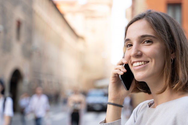 Ragazza con mezza criniera e un naso trafitto che sorride e che parla con il suo telefono cellulare