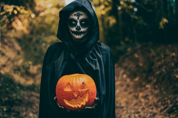 Foto ragazza con trucco di halloween, che tiene una zucca nel legno