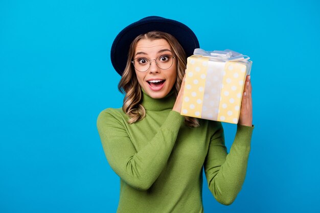 Girl with hat and glasses holding gif isolated on blue