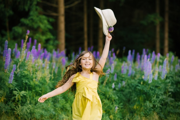 Girl with hat in hand smiling jumping up in a field of lupine