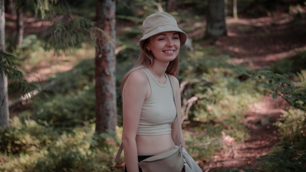 Girl with hat smiling while standing in the forest