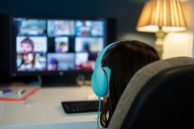 Girl with headset in front of computer screen receiving lessons at home. School at home.