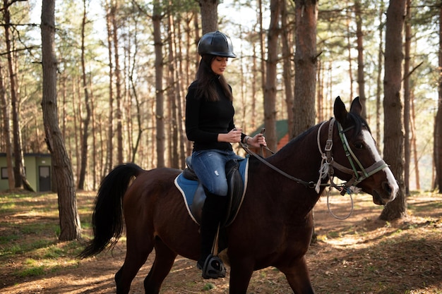 森の中で馬に乗るヘルメットを持つ少女