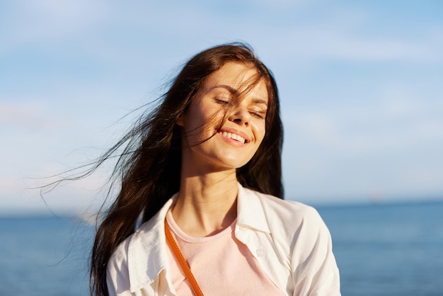 A girl with her eyes closed in the sun against an ocean backdrop smiling with teeth flying hair tanned skin relaxing traveling to the ocean