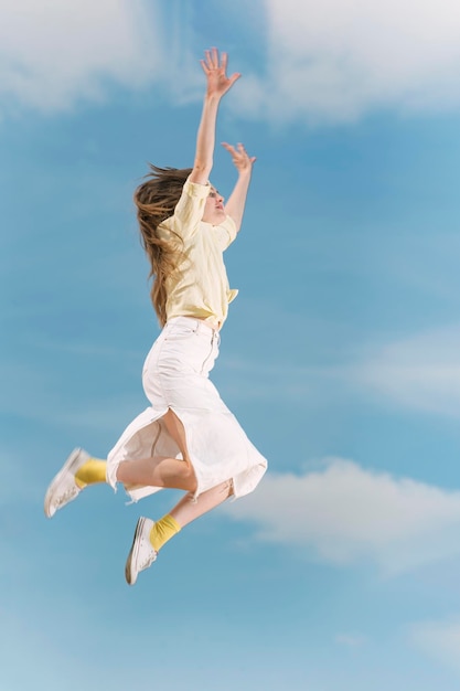 Girl with her hands raised up during jump against the blue sky Young woman flying high in blue sky