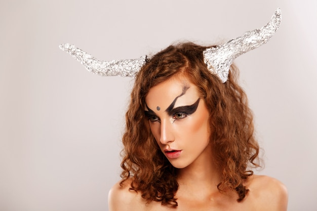 Photo girl with horns like capricornus poses before white background