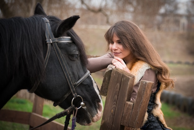 Girl with a horse on a ranch on an autumn cloudy day.