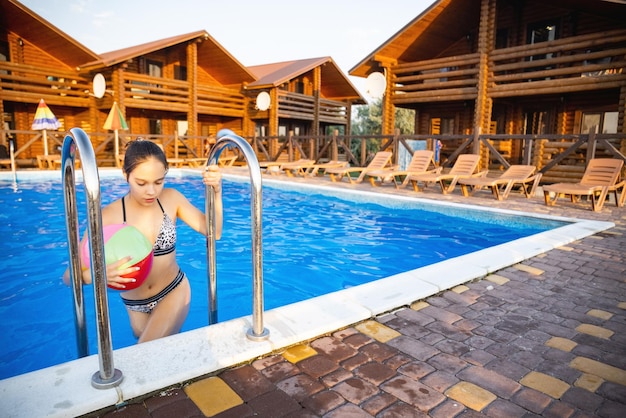 A girl with an inflatable ball in her hands climbs the stairs from the pool