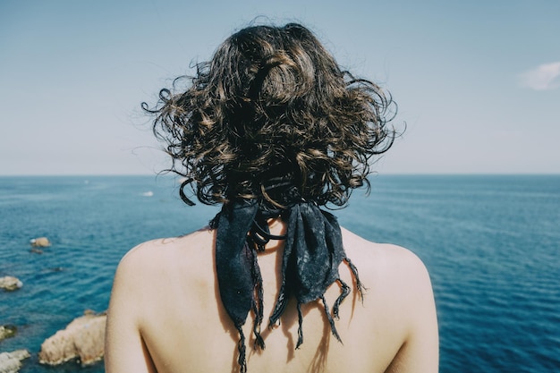 a girl with a kerchief on her neck and her back naked from behind looking at the horizon in the sea