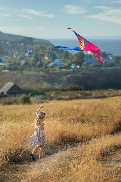 A girl with a kite in her hands runs across the field in summer Plays outdoors in the park at sunset The child plays in nature