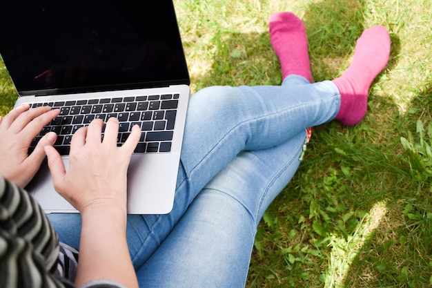Девушка с ноутбуком на зеленой траве Дистанционное обучение Ребенок работает за компьютером