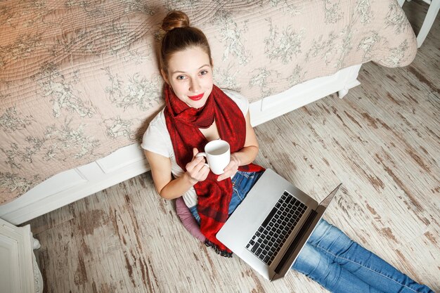 Ragazza con laptop seduta sul pavimento e bevendo