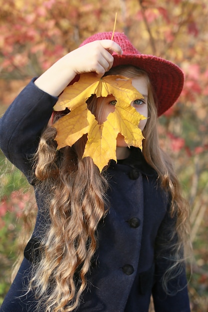 秋の公園で顔の近くの葉を持つ少女