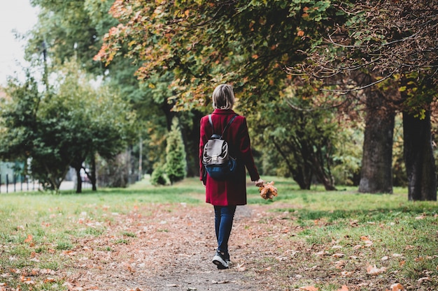 girl with leaves walking down on park alley