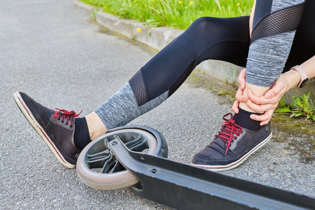 Girl with a leg injury after riding a scooter sits on the ground.