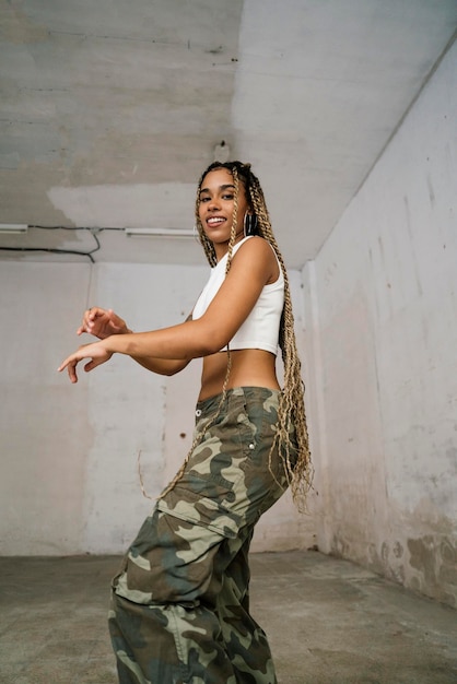 Girl with long blonde braids dancing in a black tracksuit in an abandoned warehouse while smiling and enjoying her passion and exercise