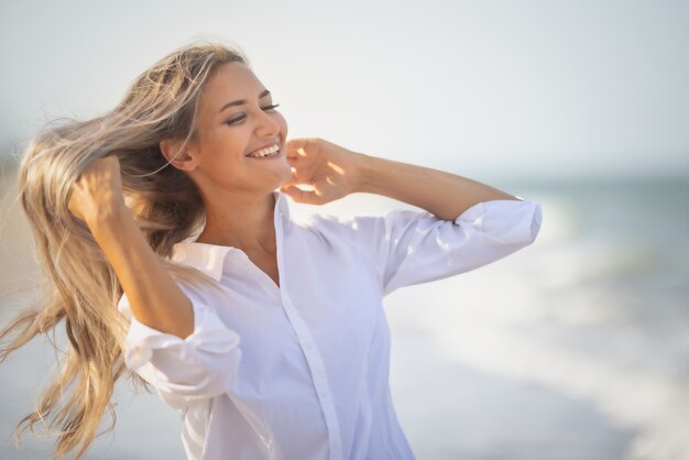 A girl with long hair in a bluish swimsuit and a shirt goes through her hair on the seashore