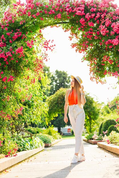 花のアーチの下の公園で長い髪とカンカン帽をかぶった女の子