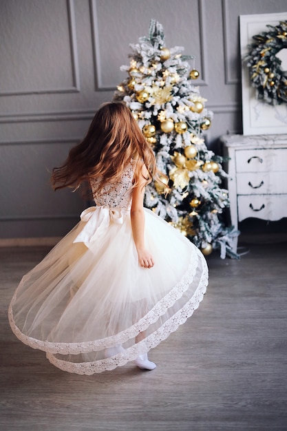 사진 흰 드레스에 긴 머리를 가진 소녀는 크리스마스 장식으로 거실에서 춤을