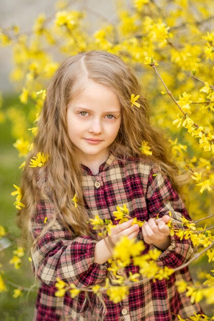 Девушка с длинными волосами в желтых цветках. ребенок на фоне форзиции. весенний портрет ребенка