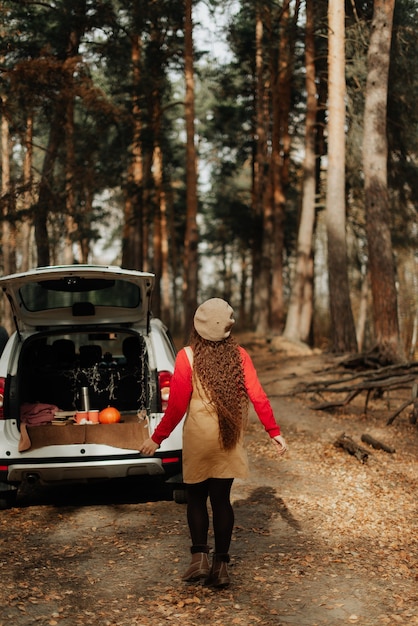 Girl with long hair in a red sweater and in a white beret walks through the woods