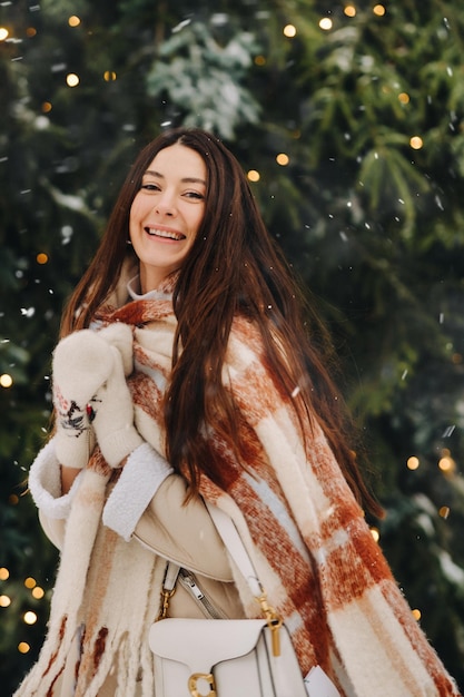 A girl with long hair in a scarf and with a white handbag walks down the street in winter