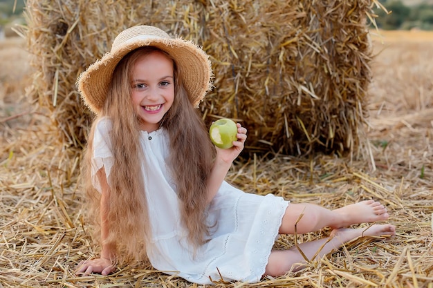 a girl with long hair in a straw hat in a wheat field with a green apple in her hands