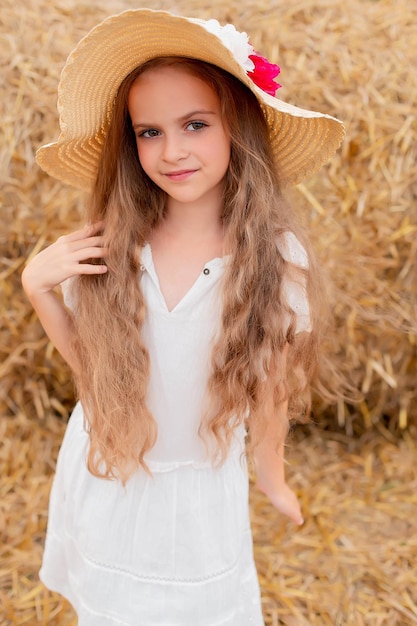 a girl with long hair in a white dress and a straw hat in a wheat field