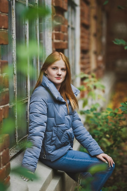 A girl with long red hair is sitting on the windowsill of an old house 2735