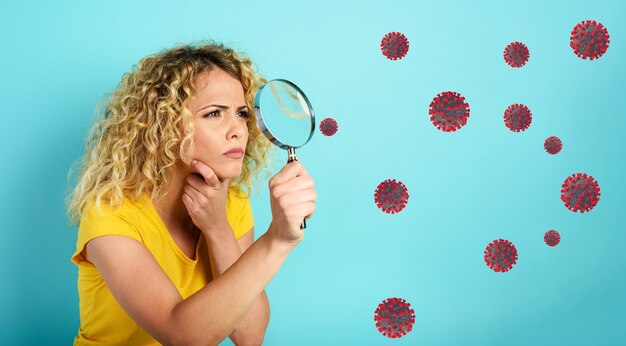 Girl with magnifier lens is distrustful about virus in air. Cyan background