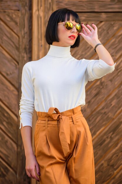 Girl with makeup posing in fashionable clothes Fashionable outfit slim tall lady Woman walk in elegant outfit Fashion and style concept Woman fashionable brunette stand outdoors wooden background