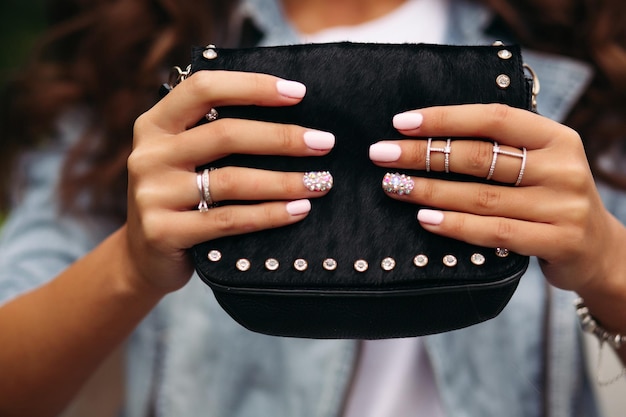 Girl with manicured nails with beautiful ornament in wedding rings holding black fur bag.