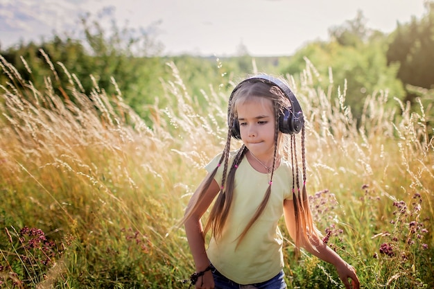 Девушка с множеством косичек и наушников слушает музыку и танцует среди цветочного поля