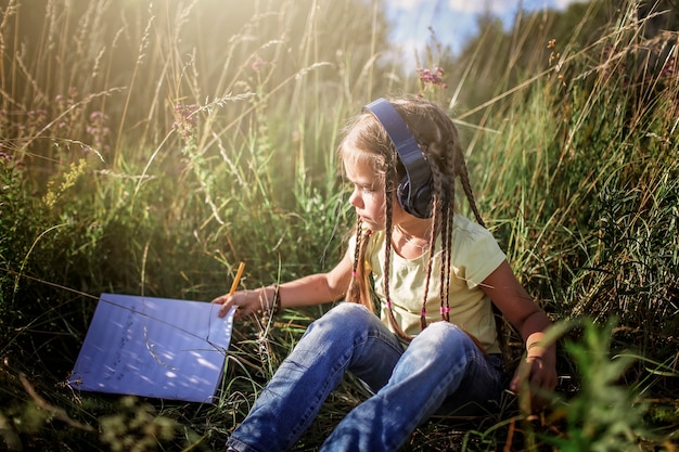 Girl with many braids and headphones listening music and writing music text at flower field