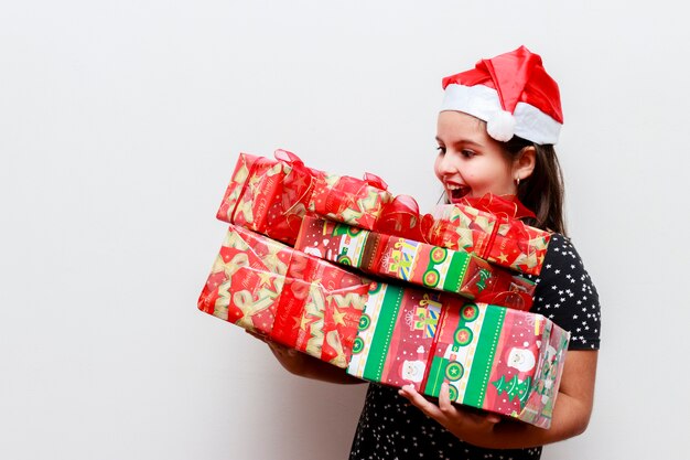 多くの贈り物とクリスマスの帽子、白い背景を持つ少女