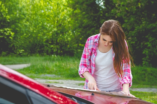 Ragazza con la mappa in mano in piedi accanto a un'auto nella foresta.