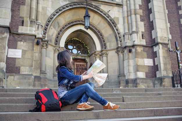 Girl with map sitting on the stairs and looks at old church