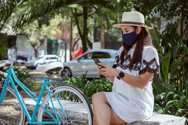 公園に座っている彼女の携帯電話をチェックするマスクを持つ少女