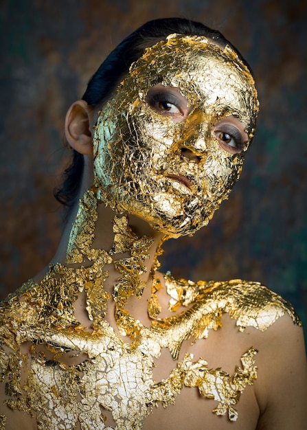 Girl with a mask on her face made of gold leaf Gloomy studio portrait of a brunette on an abstract background