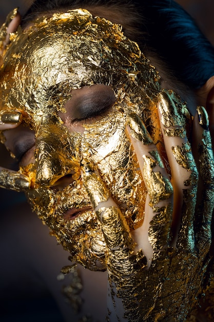 Girl with a mask on her face made of gold leaf Gloomy studio portrait of a brunette on an abstract