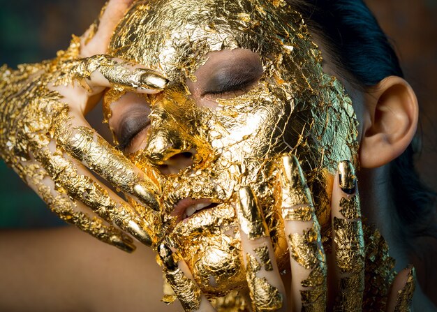 Girl with a mask on her face made of gold leaf Gloomy studio portrait of a brunette