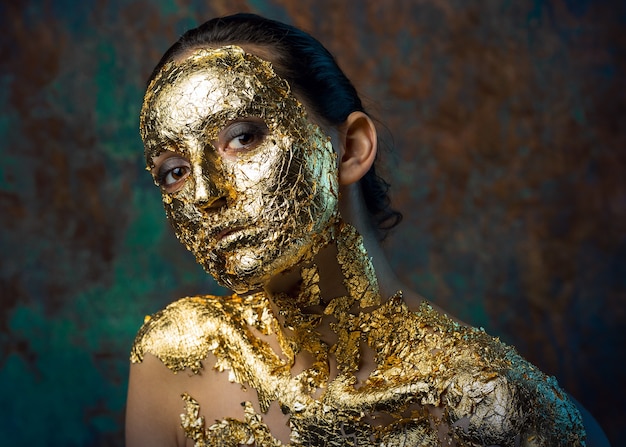 Girl with a mask on her face made of gold leaf Gloomy studio portrait of a brunette